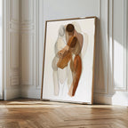 The Embrace Abstract Canvas Art, featuring two intertwined figures in earthy tones, leans against a white paneled wall on a wooden floor, adding modern elegance and style to bright living room decor.