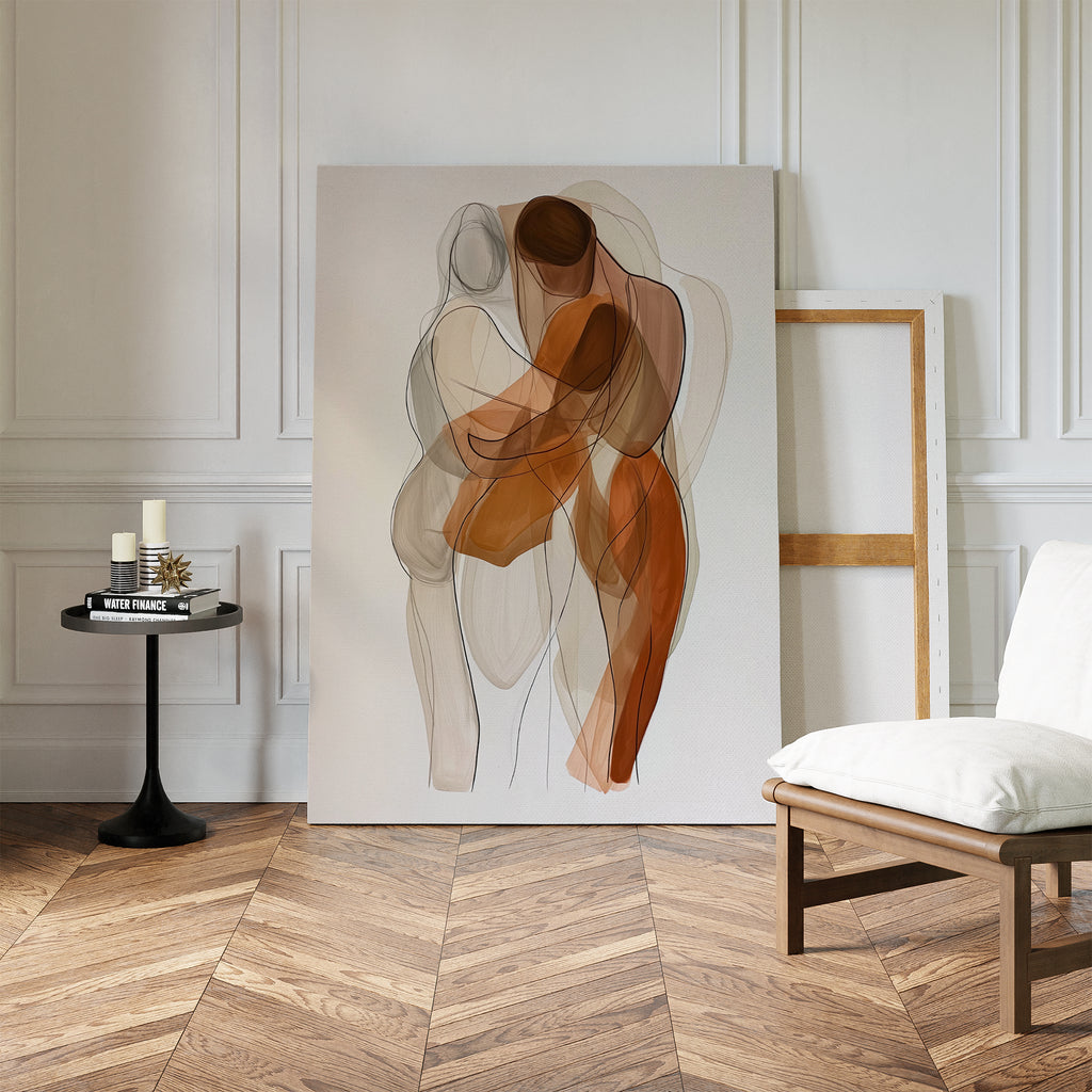 The Embrace Abstract Canvas Art, featuring two intertwined human figures with transparent shapes, leans against a white paneled wall. Nearby sit a chair, an empty frame, and a side table with candles and books for a minimalist look.