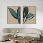 Minimalist living room decor with a curved beige sofa, round wooden coffee table, small flower vases, and the Emerald Poise Set of 2—large botanical wall art prints of green leaves on tan backgrounds above the sofa.