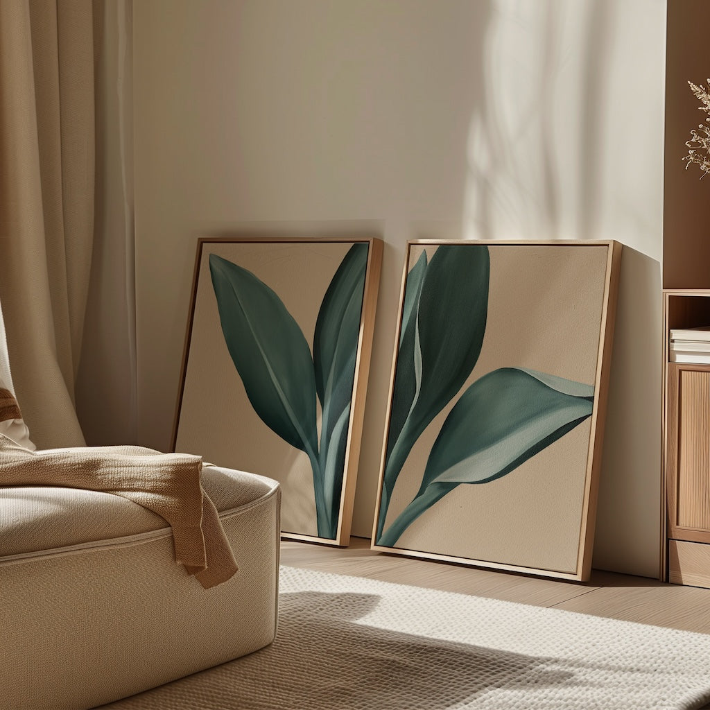 The Emerald Poise Set of 2 features framed minimalist wall art prints with green leaves, leaning against a beige wall in a sunlit room with a cream armchair and neutral decor for a calm, modern look.