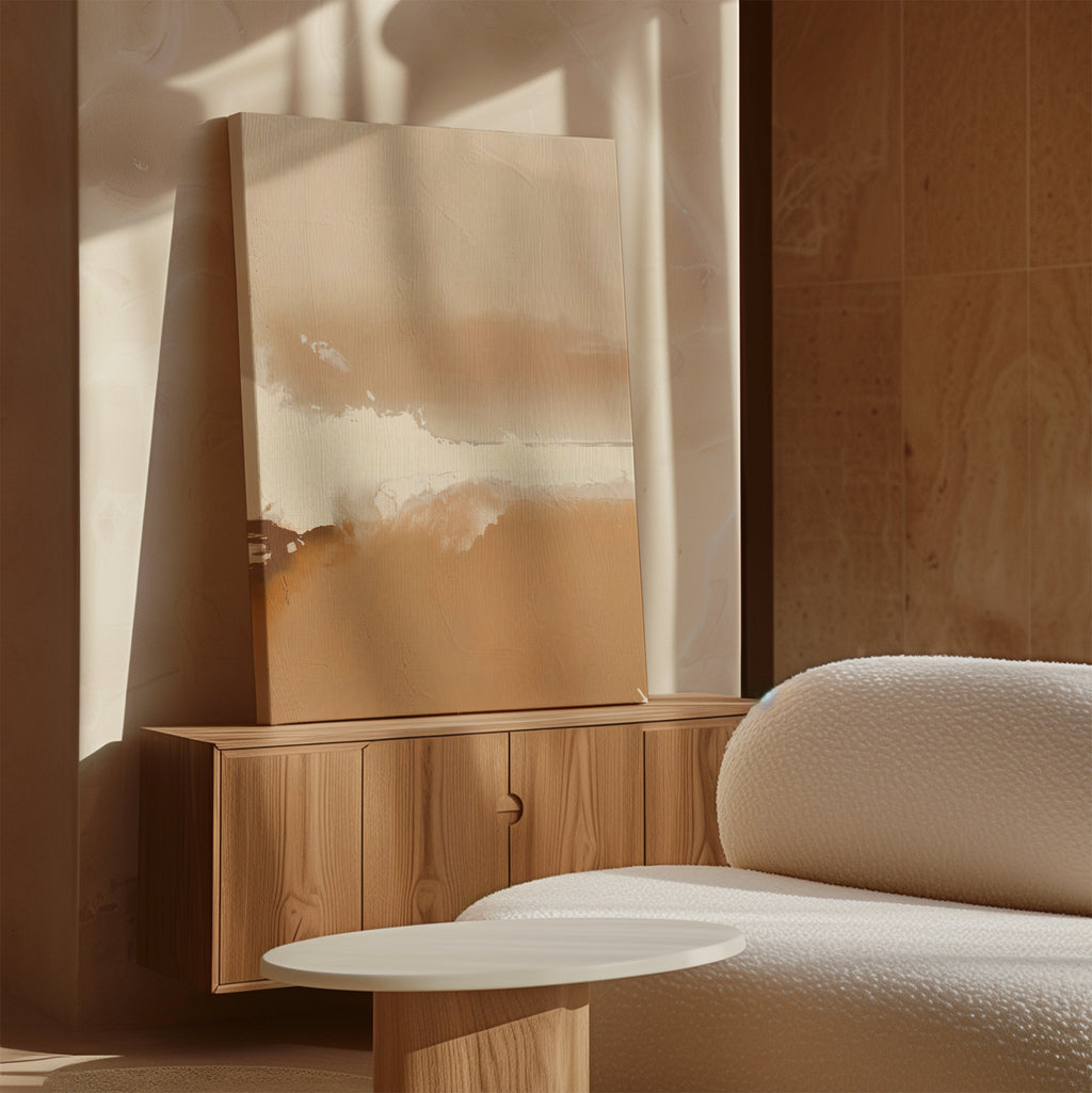 A minimalist living room with warm beige tones features a wooden sideboard, the Ethereal Plains Abstract Canvas Art in soft neutrals, a round white coffee table, and a textured white sofa bathed in natural sunlight.