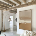 A modern living room with exposed wooden beams, white walls, and the Ethereal Plains Abstract Canvas Art above a white sofa. A curved floor lamp and natural light enhance the bright, inviting decor.
