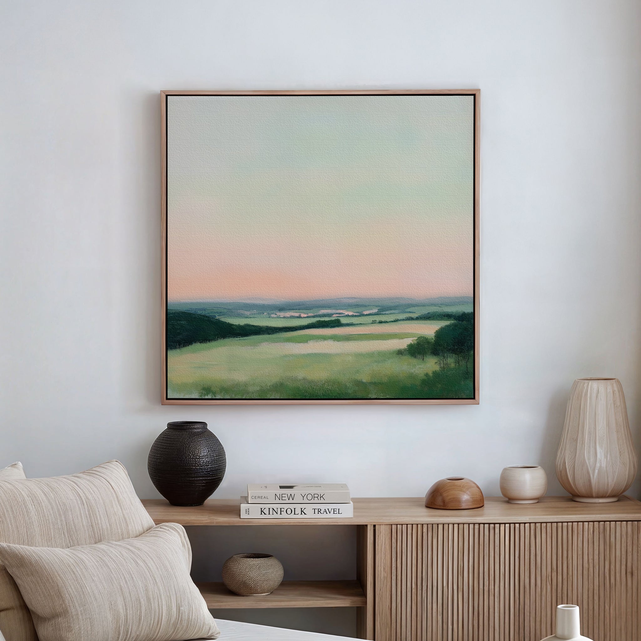 The Evening Hues Abstract Canvas Art hangs above a wooden sideboard adorned with vases, a candle, and stacked books, creating a serene setting with neutral tones and minimalist living room decor.