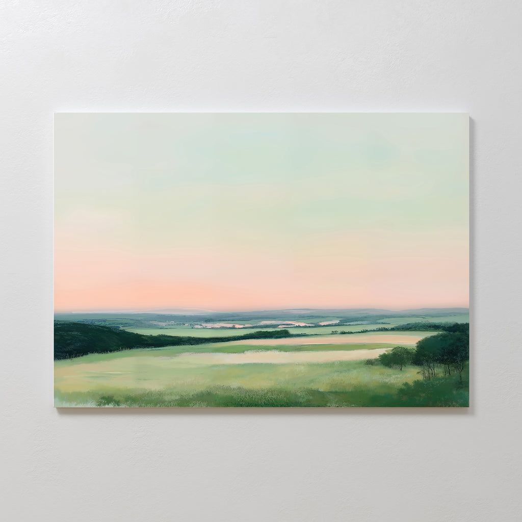 The Evening Hues Canvas Art – Horizontal features a serene landscape with green fields, distant hills, and a pastel sky at sunrise or sunset—ideal as large wall art for elegant living room decor. Displayed on a white wall.