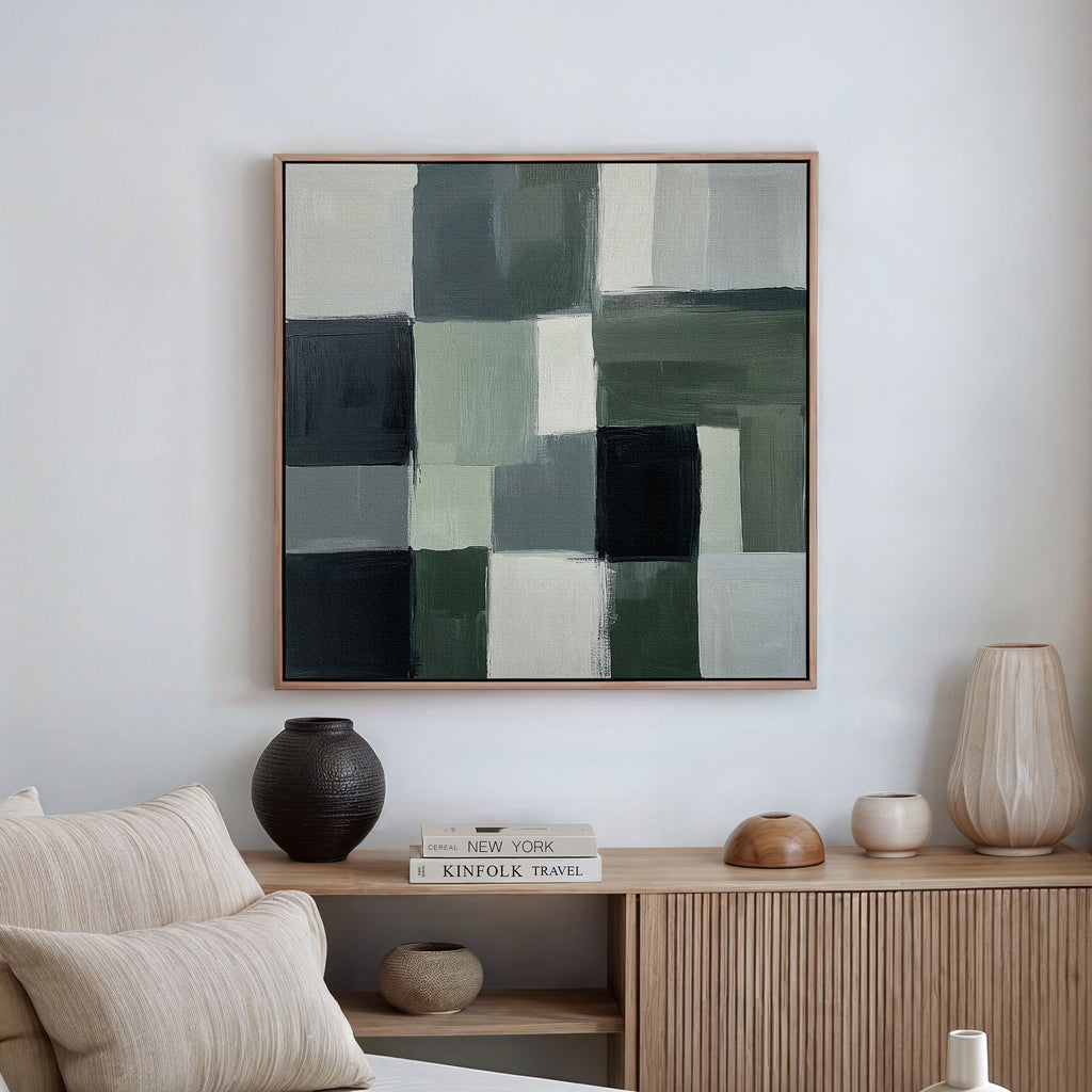 A modern living room showcases a minimalist wooden sideboard and neutral decor, with the Evergreen Abstract Canvas Art—featuring green, white, gray, and black geometric blocks—hanging on the white wall above.