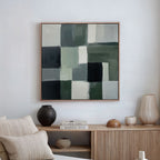 A modern living room showcases a minimalist wooden sideboard and neutral decor, with the Evergreen Abstract Canvas Art—featuring green, white, gray, and black geometric blocks—hanging on the white wall above.