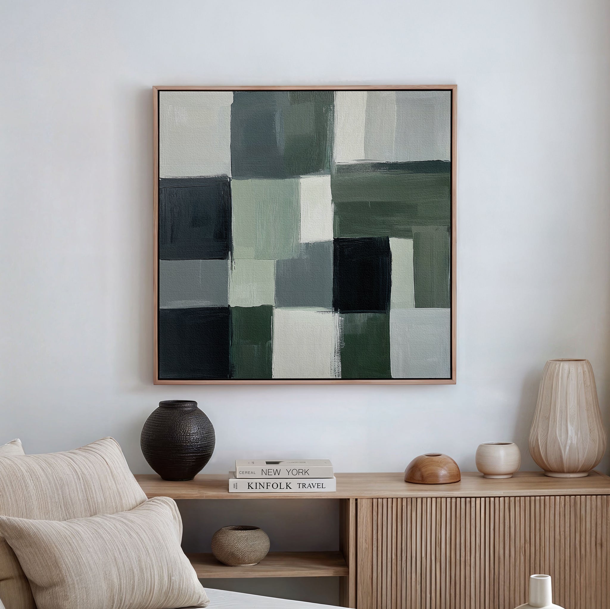 A modern living room showcases a minimalist wooden sideboard and neutral decor, with the Evergreen Abstract Canvas Art—featuring green, white, gray, and black geometric blocks—hanging on the white wall above.