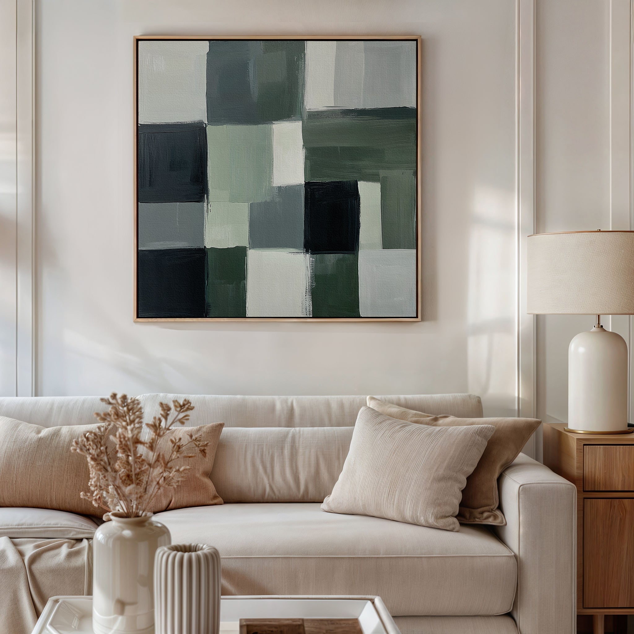 A modern living room with a beige sofa, cream cushions, a wooden side table with a white lamp, dried flowers in a vase, and the Evergreen Abstract Canvas Art in green and black hanging above the sofa.