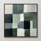 The Evergreen Abstract Canvas Art showcases a grid of green, gray, black, and white rectangles with textured brushstrokes for a layered look. Framed in thin dark wood, this modern abstract piece stands out against a white wall.