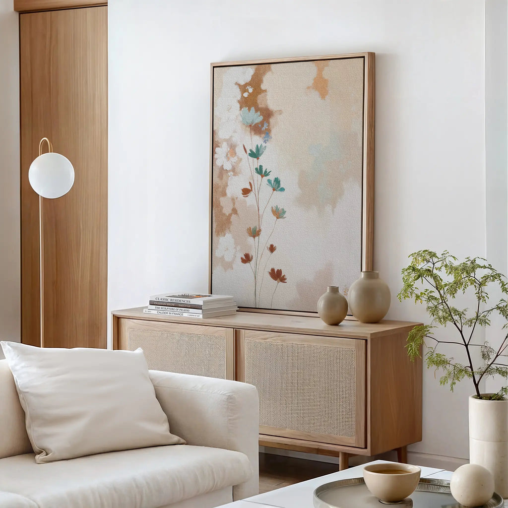 A minimalist living room features a light wood sideboard, neutral vases, books, vintage-inspired decor, a white sofa with cushions, modern floor lamp, potted plant, and the soft palette is complemented by Faded Flora Canvas Art on the wall.