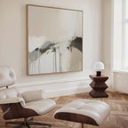 A modern minimalist living room decor featuring a white lounge chair and ottoman, a wooden side table with lamp, and the Faded Memory Canvas Art in beige, black, and gray tones displayed on a cream wall.