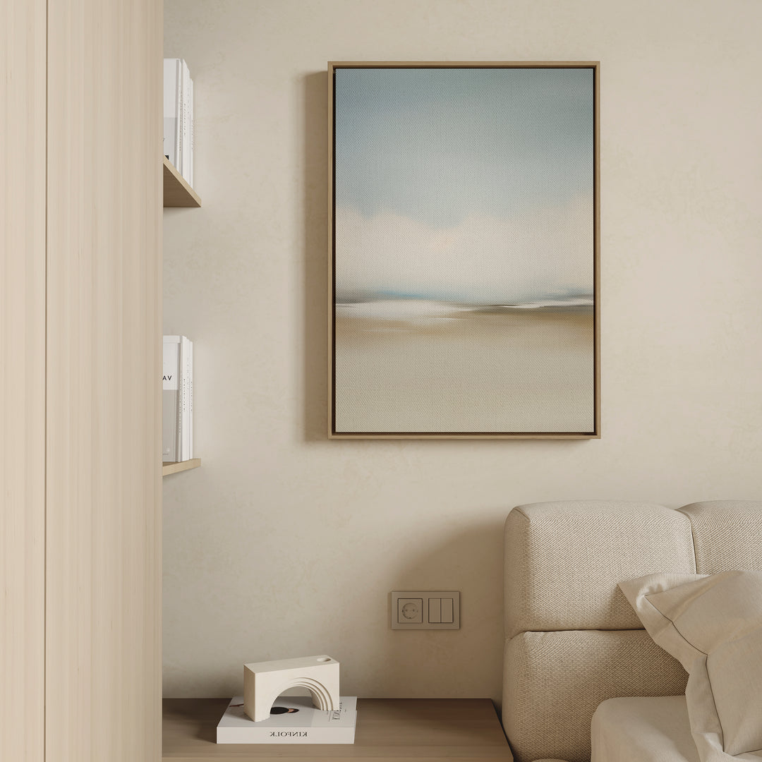 A minimalistic living room corner features a textured beige sofa, wall outlet, bookshelf with books, small white geometric decor, and modern wall decor—Faded Silence Canvas Art in soft blue and beige tones on a light wall.