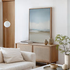 A minimalist living room with a beige sofa, light wood sideboard, neutral vases, stacked books, a potted plant, and a round white pendant lamp features the Faded Silence Canvas Art on white walls.