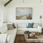 A cozy living room with a white sectional sofa, assorted pillows, a rustic wooden coffee table, and the Far Light Canvas Art featuring a country road on the shiplap wall. Natural light streams in from the left.