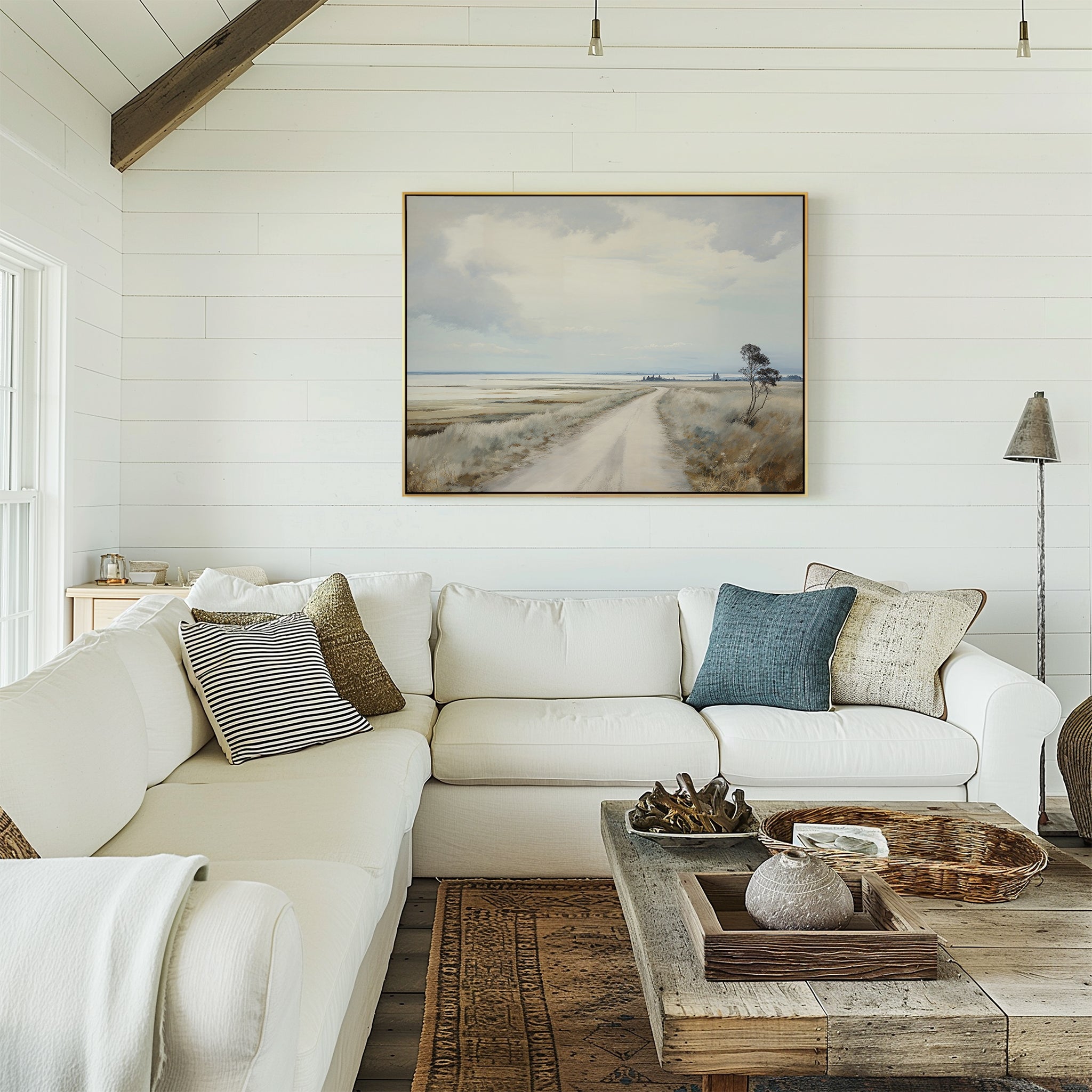 A cozy living room with a white sectional sofa, assorted pillows, a rustic wooden coffee table, and the Far Light Canvas Art featuring a country road on the shiplap wall. Natural light streams in from the left.