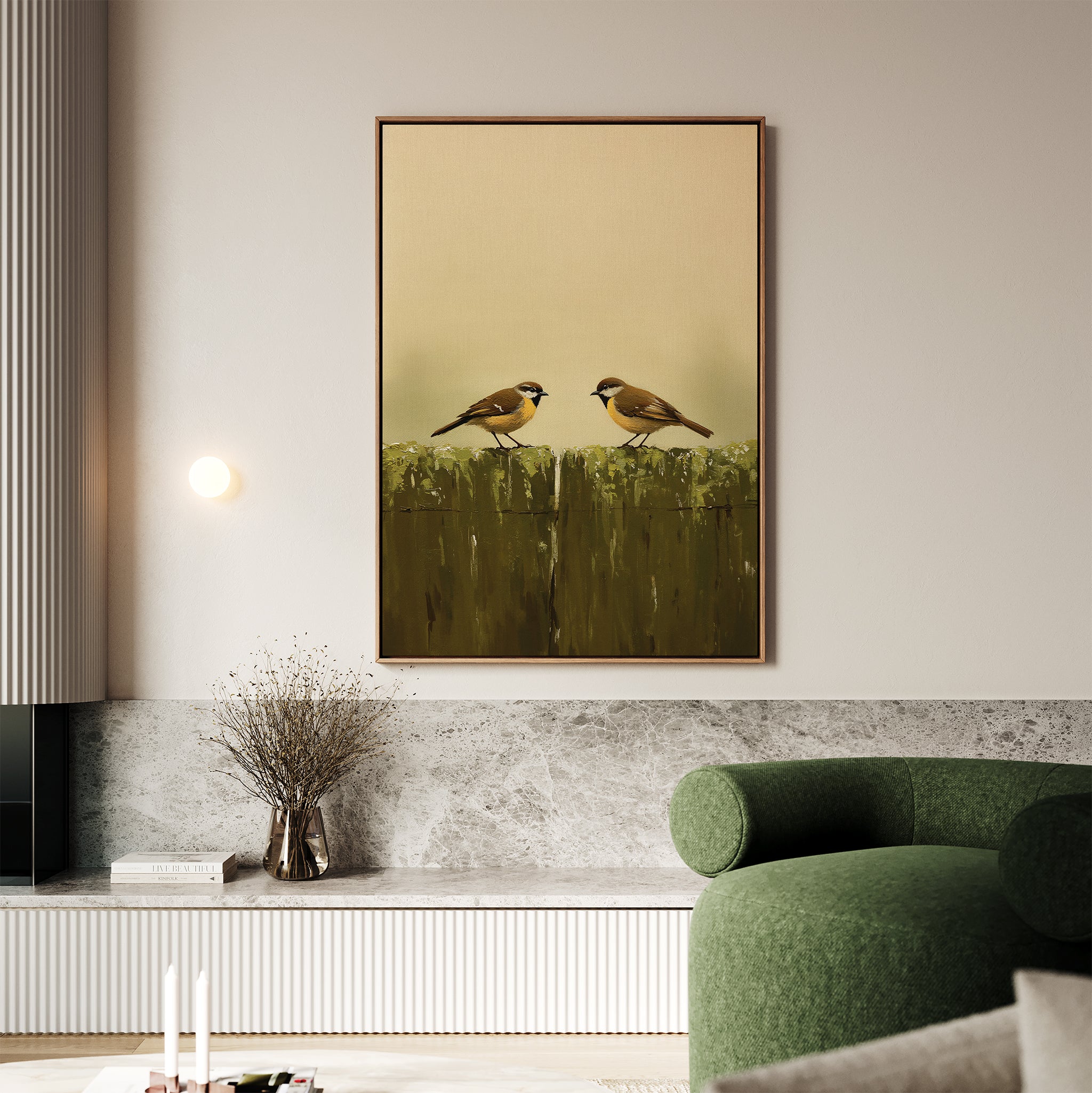 A modern living room with a green sofa, marble shelf holding a vase of dried branches, and the framed Fence Companions Canvas Art—depicting two birds on a mossy fence—adds an elegant, nature-inspired accent above.