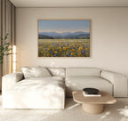 A modern living room with a light beige sectional sofa, a wooden coffee table, and the Fields of Color Canvas Art depicting a wildflower field with mountains hanging on the neutral-colored wall.