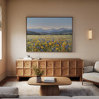 A cozy living room with a wooden coffee table, beige sofa, patterned sideboard, and the Fields of Color Canvas Art featuring wildflower fields and mountains. A vase with flowers on the table completes the modern decor.