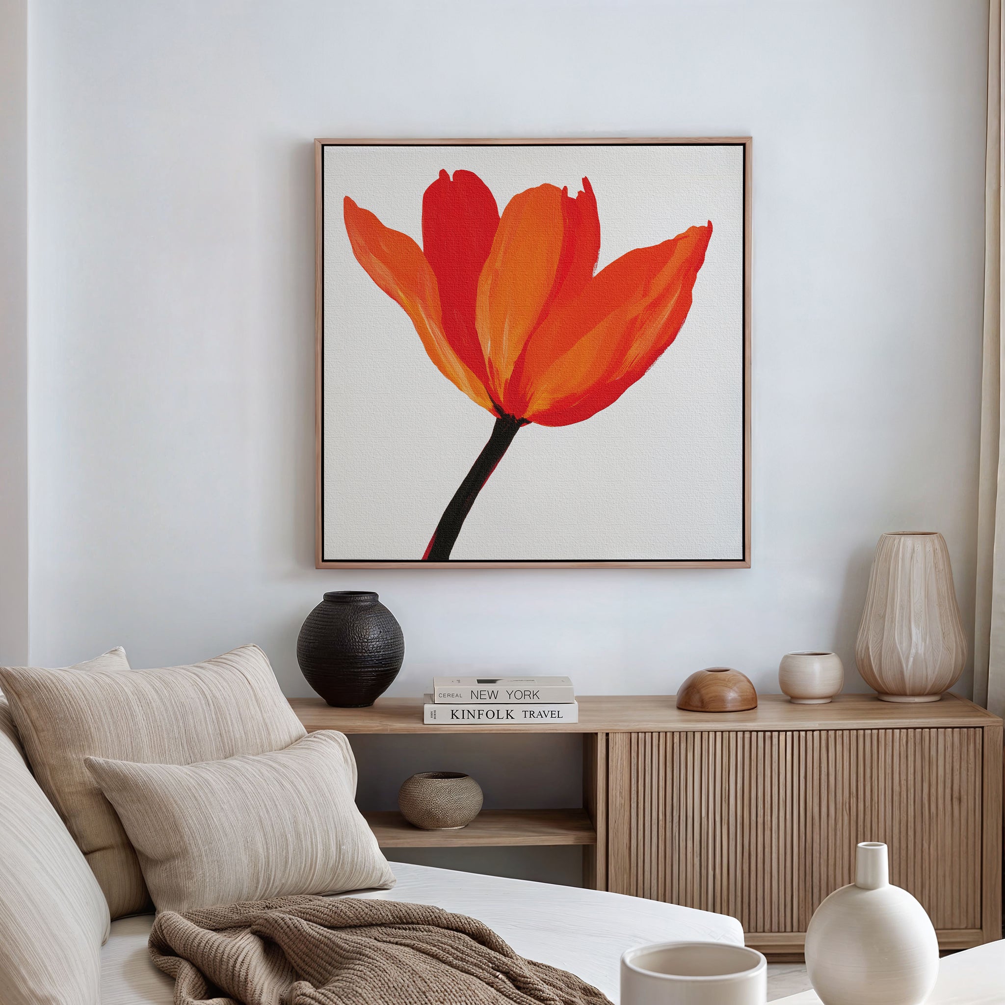 A minimalist living room featuring a beige sofa with pillows, wooden sideboard, ceramic vases, stacked books, and eye-catching Flame Tulip Canvas Art. Soft natural light from a window enhances the chic decor.