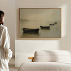 A woman stands in a minimalist room, gazing at the Floating Dreams Canvas Art—a painting of four rowboats on calm water—displayed above a beige upholstered sofa.