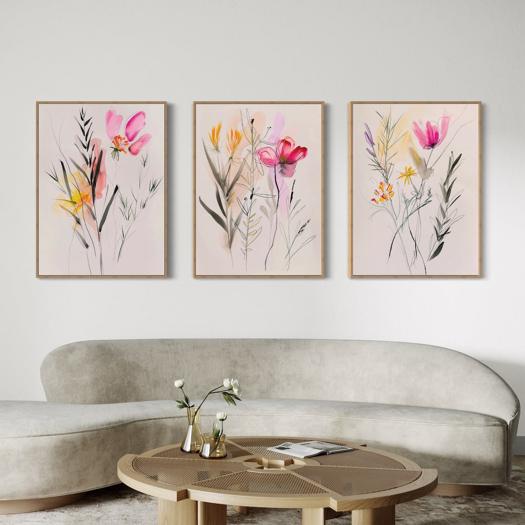 A modern living room featuring a curved beige sofa, round wooden coffee table, and the Floral Harmony Set of 3 prints in pink, yellow, and red on a white wall—perfect for chic living room decor.
