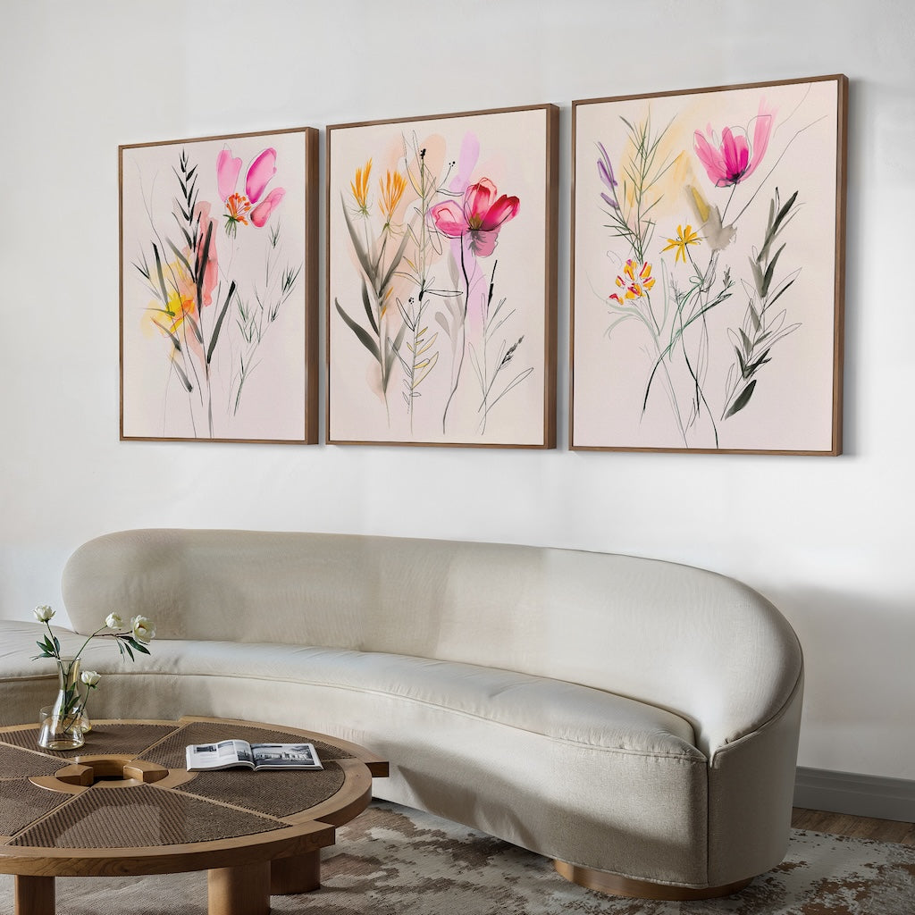 A modern living room featuring a curved light beige sofa, a round wooden coffee table, and the Floral Harmony Set of 3 vibrant floral framed paintings above the sofa—perfect for elevating your living room decor.
