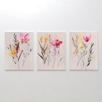 The Floral Harmony Set of 3 displays abstract wildflowers in pink, yellow, and red on canvas, arranged side by side. These minimalistic floral pieces are ideal as modern living room decor.
