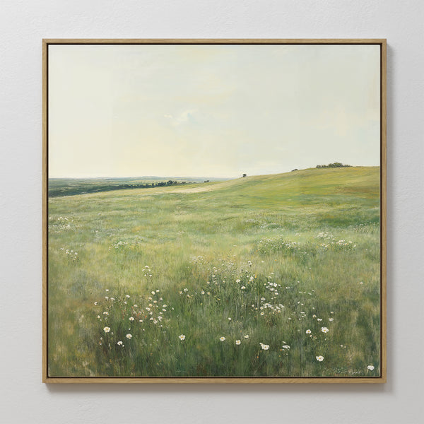 The Floral Meadow Canvas Art, featuring a sunlit grassy meadow with white wildflowers, rolling hills, and a distant tree beneath a pale sky, hangs on a white wall—an ideal touch for living room decor.