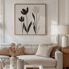 A neutral-toned living room features a beige sofa, light cushions, dried flowers in a vase, a table lamp, and the Floral Simplicity Canvas Art—minimalist black and beige wall art—hanging above the sofa.
