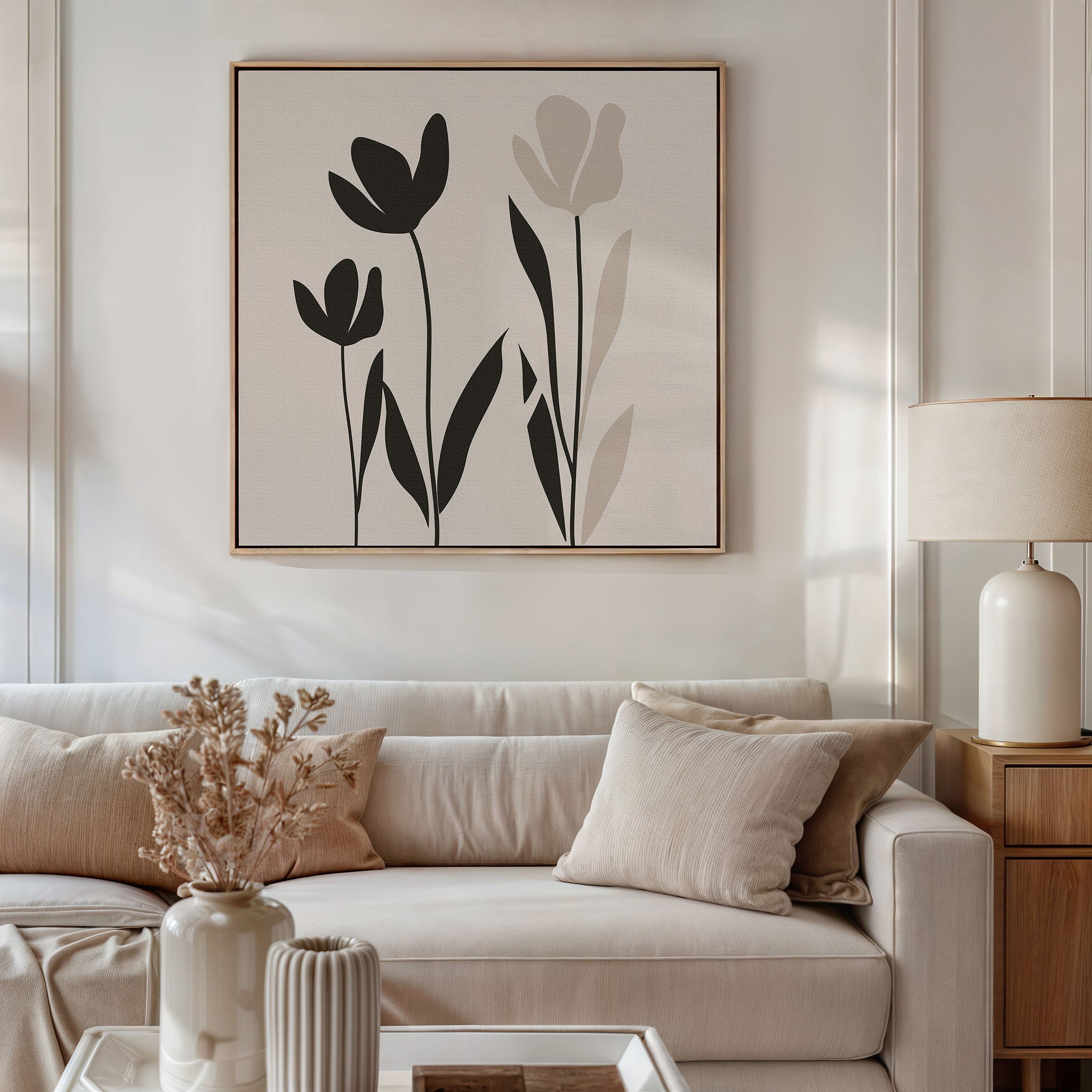 A neutral-toned living room features a beige sofa, light cushions, dried flowers in a vase, a table lamp, and the Floral Simplicity Canvas Art—minimalist black and beige wall art—hanging above the sofa.
