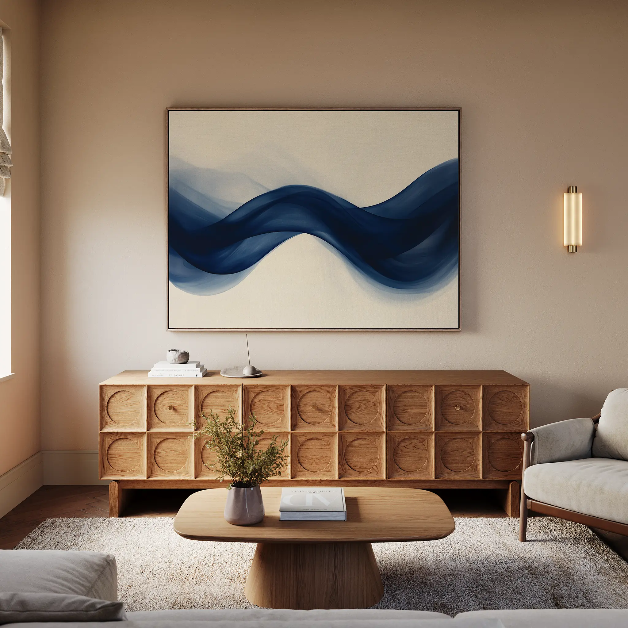 A modern living room with a light sofa, wooden coffee table, decorative credenza, and Flowing Indigo Canvas Art—a striking blue abstract wave painting. A small plant and books complete the stylish minimalist decor.