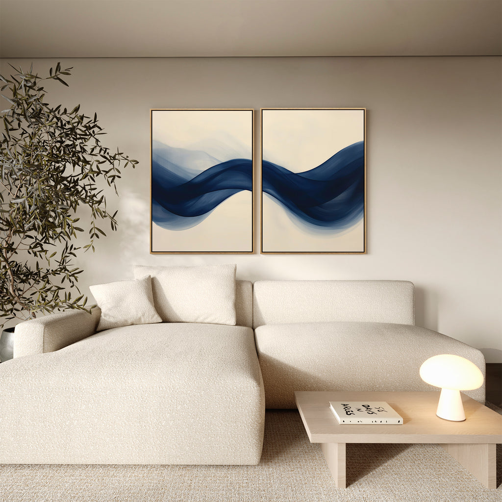 A modern living room with a cream sectional, light wood coffee table, indoor plant, and the Flowing Indigo Set of 2 abstract blue wave paintings on a beige wall—ideal for sleek minimalist and stylish living room decor.
