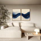 A modern living room with a cream sectional, light wood coffee table, indoor plant, and the Flowing Indigo Set of 2 abstract blue wave paintings on a beige wall—ideal for sleek minimalist and stylish living room decor.