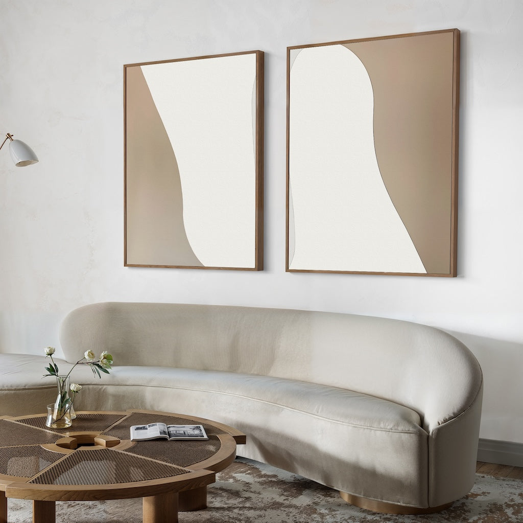 A modern living room with a curved light gray sofa, a round wooden coffee table, a wall-mounted lamp, and the Flowing Silhouettes Set of 2 minimalist wall art in beige and white as stylish decor above the sofa.