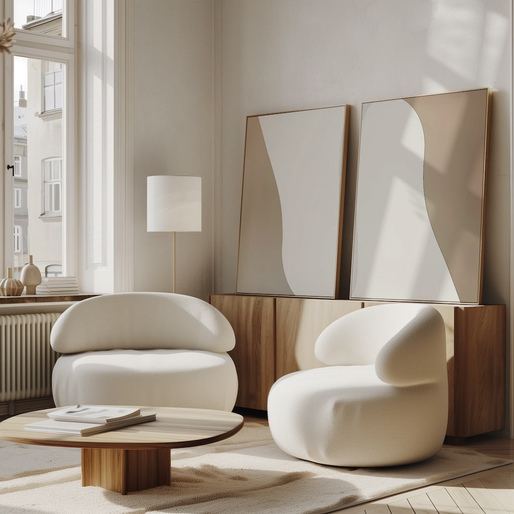 A modern living room with two rounded white armchairs, a low wooden coffee table, abstract mirrors on a wooden sideboard, large windows, and neutral decor featuring the Flowing Silhouettes Set of 2 wall art.