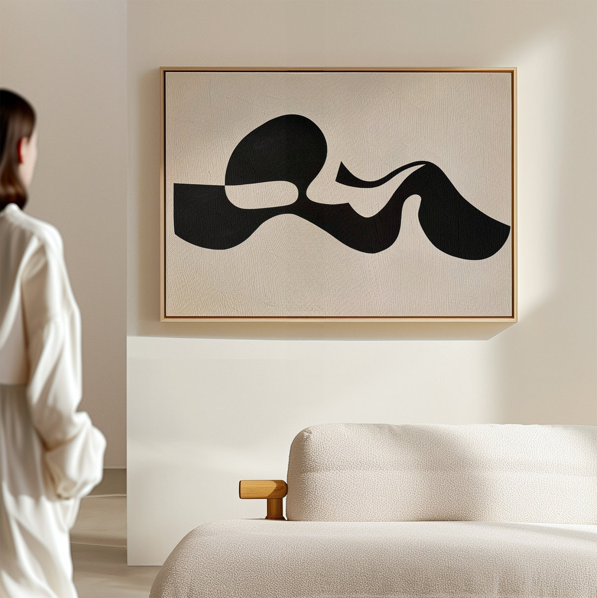 A person in white stands in a minimal, modern room with a cream sofa. Sunlight casts soft shadows across the walls, highlighting the Fluid Forms Abstract Canvas Art displayed prominently above the furniture.