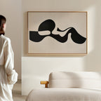 A person in white stands in a minimal, modern room with a cream sofa. Sunlight casts soft shadows across the walls, highlighting the Fluid Forms Abstract Canvas Art displayed prominently above the furniture.