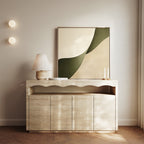 A minimalist console table with a wave-like edge holds a ceramic lamp, two tall candles, and the Forest Flow Canvas Art featuring beige and green shapes, set against a light wall with two round lights.