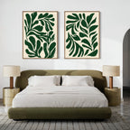 A modern bedroom with a green upholstered bed, white bedding, two bedside tables with matching lamps, and two large Forest Leaves Set of 2 botanical wall art prints displayed above the bed.