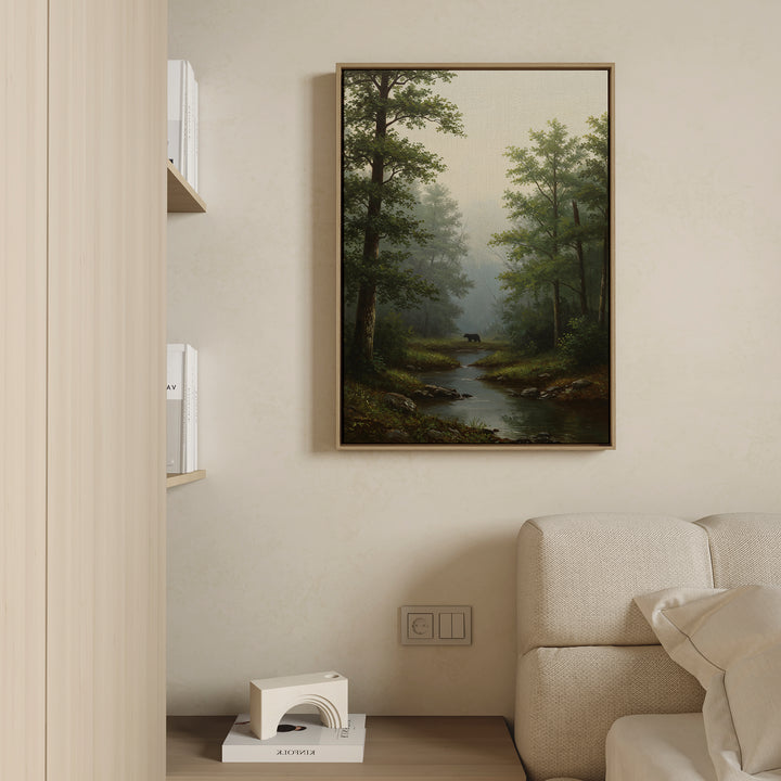 The Forest Passage Canvas Art, a framed landscape print of a forest with a stream, hangs above a beige sofa on a light wall, with part of a bookshelf and decor item in view for peaceful forest-inspired ambiance.
