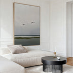 A modern, minimalist living room features a cream sofa, black round coffee table, candles, cup, and serene decor highlighted by the Freeflight Canvas Art—large wall art depicting an ocean view with two birds flying.