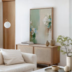 A modern living room features a light wood sideboard with vases, books, and the Garden Bloom Canvas Art. A white sofa, round lamp, and potted plant complete the minimalist decor.