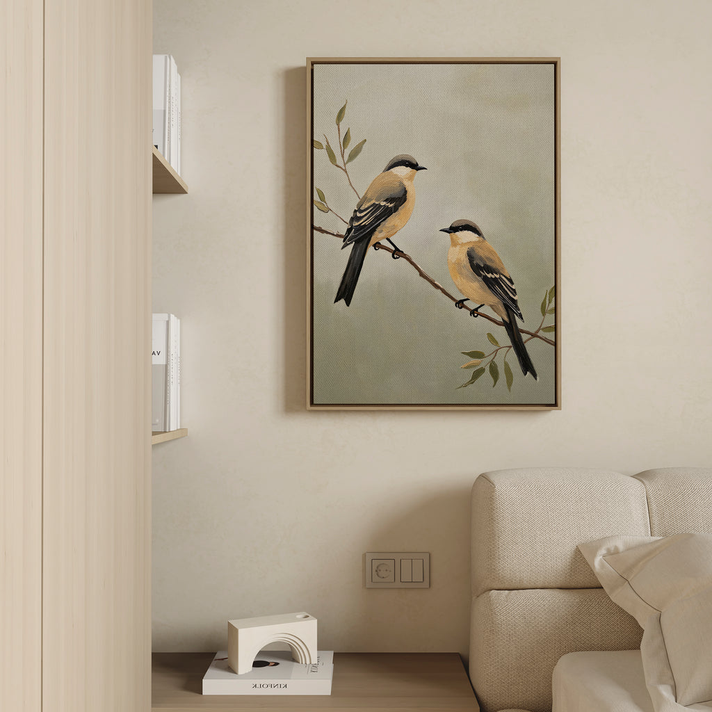 The Garden Pair Canvas Art, featuring two yellow and black birds on a branch, hangs above a cream sofa and brings Nordic Park charm to the living room. Books on a nearby shelf complete this modern, minimal space.