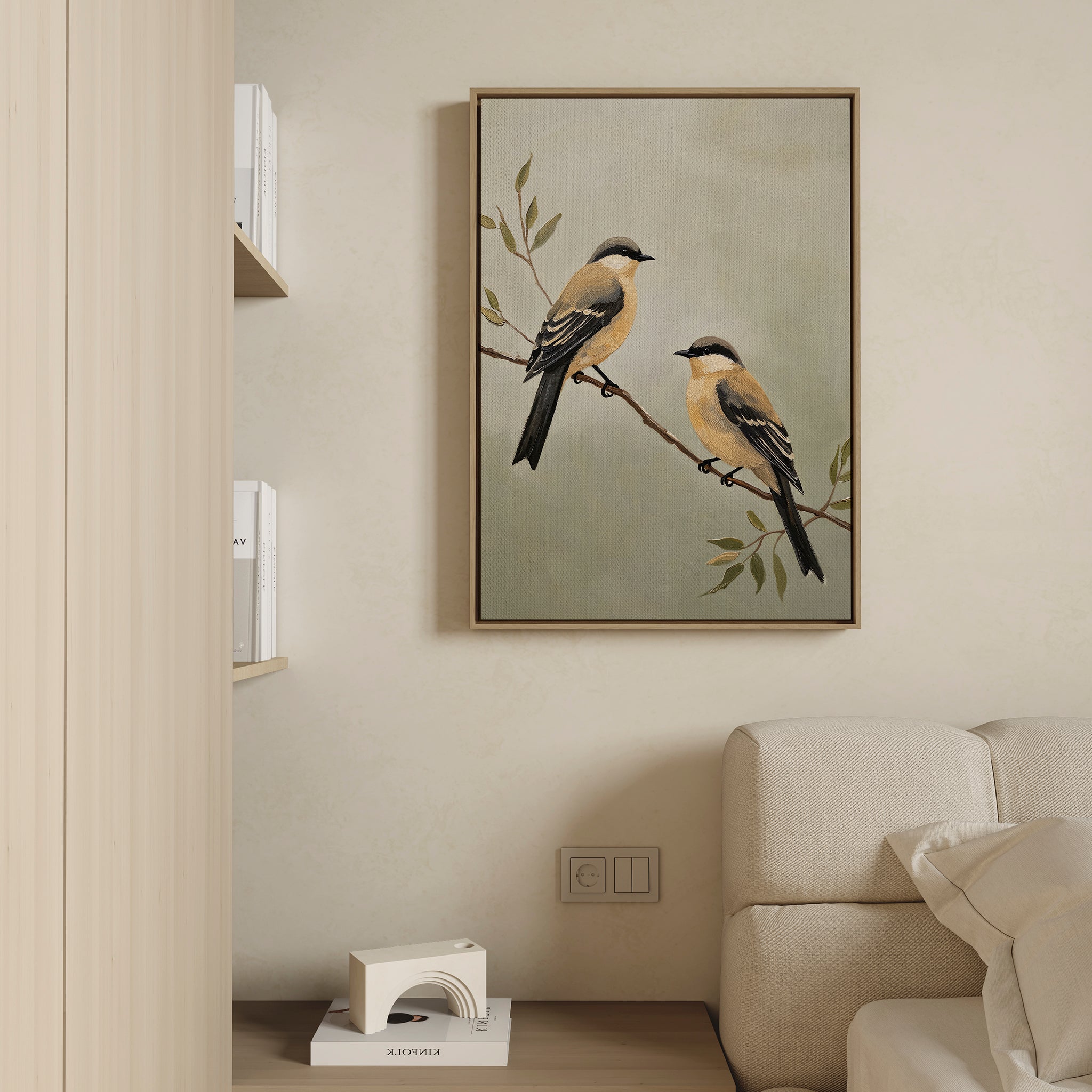 The Garden Pair Canvas Art, featuring two yellow and black birds on a branch, hangs above a cream sofa and brings Nordic Park charm to the living room. Books on a nearby shelf complete this modern, minimal space.