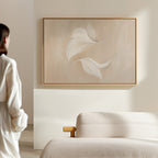 A person in white stands in a minimal, light-filled room with a beige sofa and the Garden Spectrum Abstract Canvas Art—a perfect choice to elevate your living room decor.