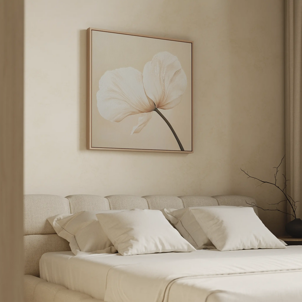 A minimal beige bedroom features a cushioned headboard, neatly made bed with white pillows, and the Gentle Poppy Canvas Art—a large floral print with two white petals—displayed above the bed.