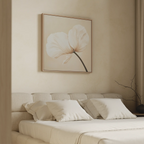 A minimal beige bedroom features a cushioned headboard, neatly made bed with white pillows, and the Gentle Poppy Canvas Art—a large floral print with two white petals—displayed above the bed.