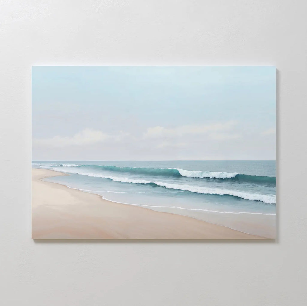 Gentle Surf Canvas Art depicts calm waves on a sandy beach beneath a cloudy sky, making it ideal coastal wall art for bedroom decor, beautifully displayed on a plain, light-colored wall.