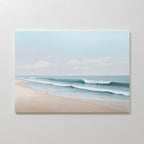 Gentle Surf Canvas Art depicts calm waves on a sandy beach beneath a cloudy sky, making it ideal coastal wall art for bedroom decor, beautifully displayed on a plain, light-colored wall.