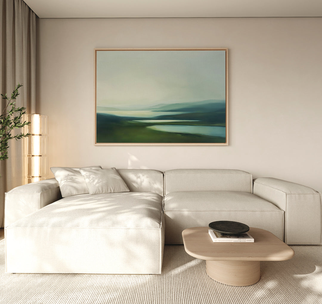 A light beige sectional and wooden coffee table with a black bowl pair beautifully with tall sheer curtains and the Gentle Valleys Canvas Art – Horizontal, a large landscape painting in blue and green tones that elevates tranquil living room decor.